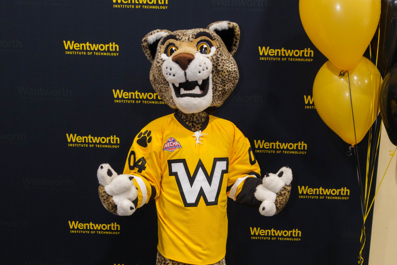 Ruggles the Leopard Mascot poses in front of the Wentworth Step-and-Repeat sign