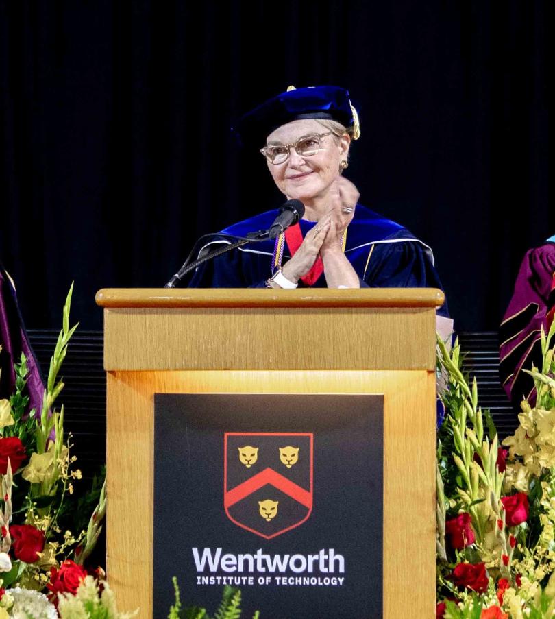 woman in graduation robe speaking at podium