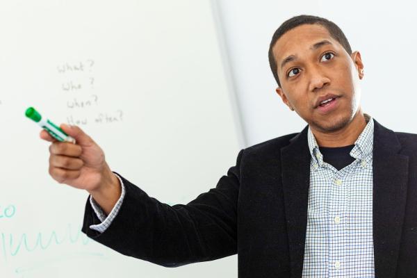 A man in mid speech in front of a white board