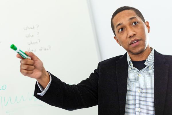 A man in mid speech in front of a white board 