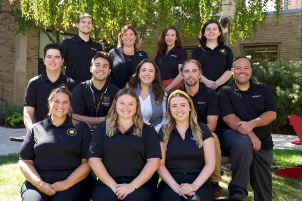 The staff of admissions and student ambassadors pose together outside on the quad on a sunny day