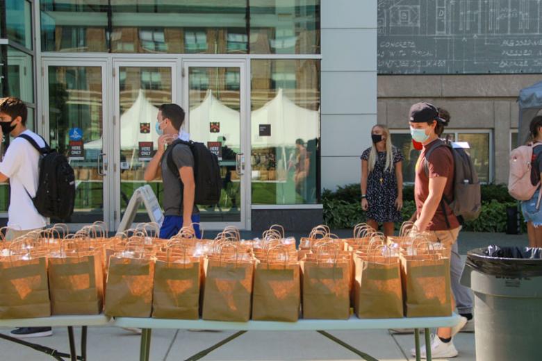 A few students file past the paper bag lunches set out for them on a table in the Quad.