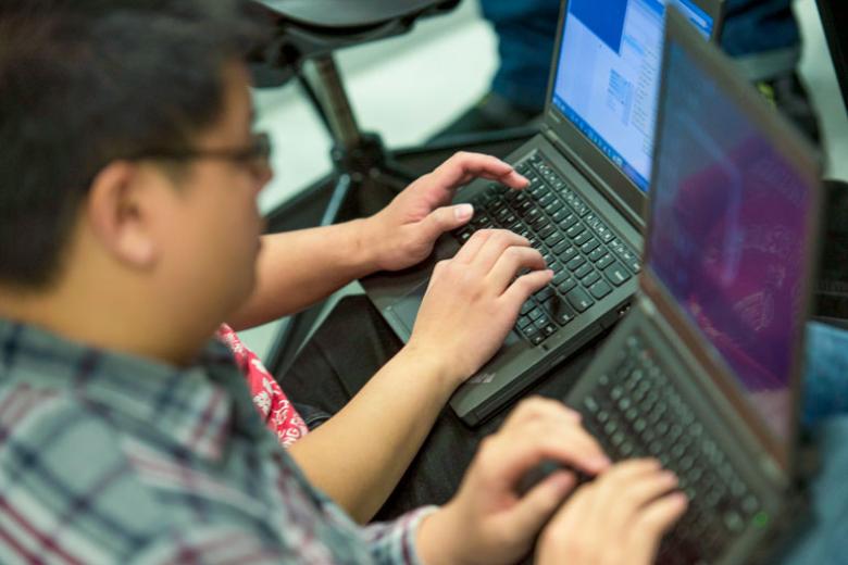 A closeup of a males student as he works on his laptop.