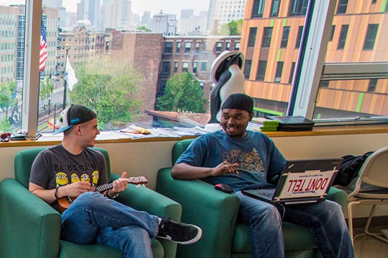 Two males students having a conversation are seated in the dorm common area