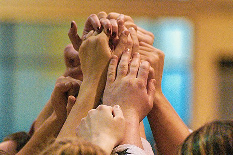 A group of students clasp hands above their head in celebration. 