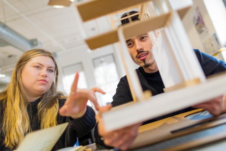 A female and male student examine an architectural model. 