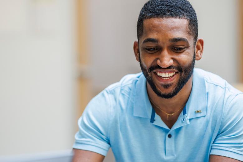 A Wentworth student of color smiles while looking at his laptop.