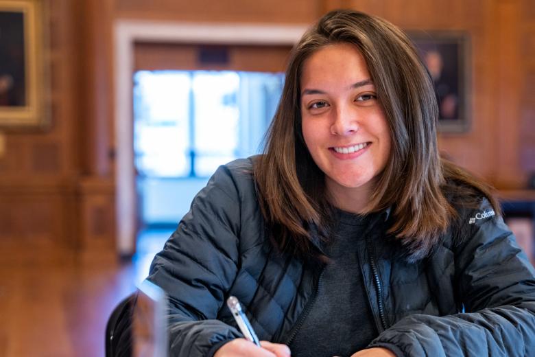 A woman smiles while holding a pencil at a table