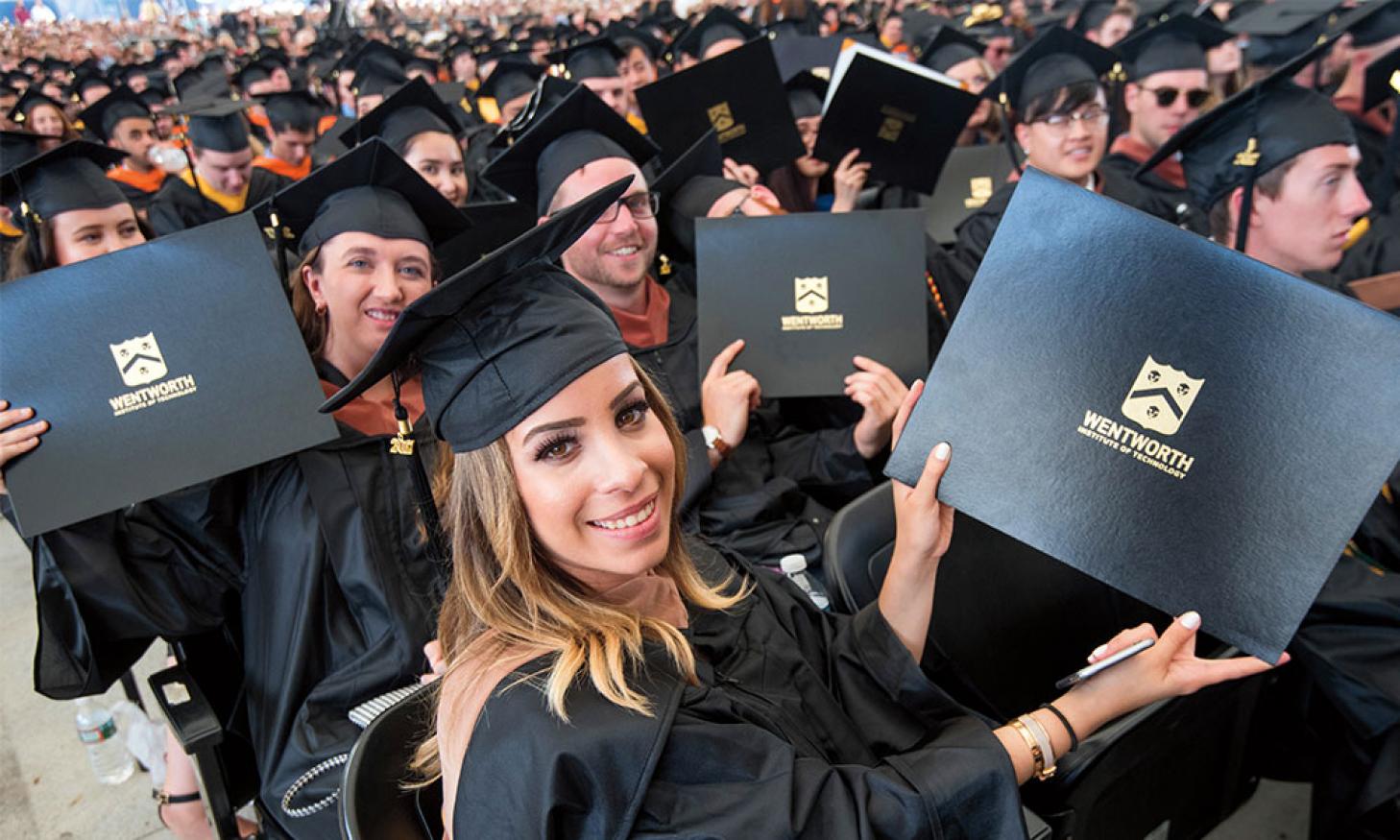 A picture of students in cap and gown holding up their diplomas 