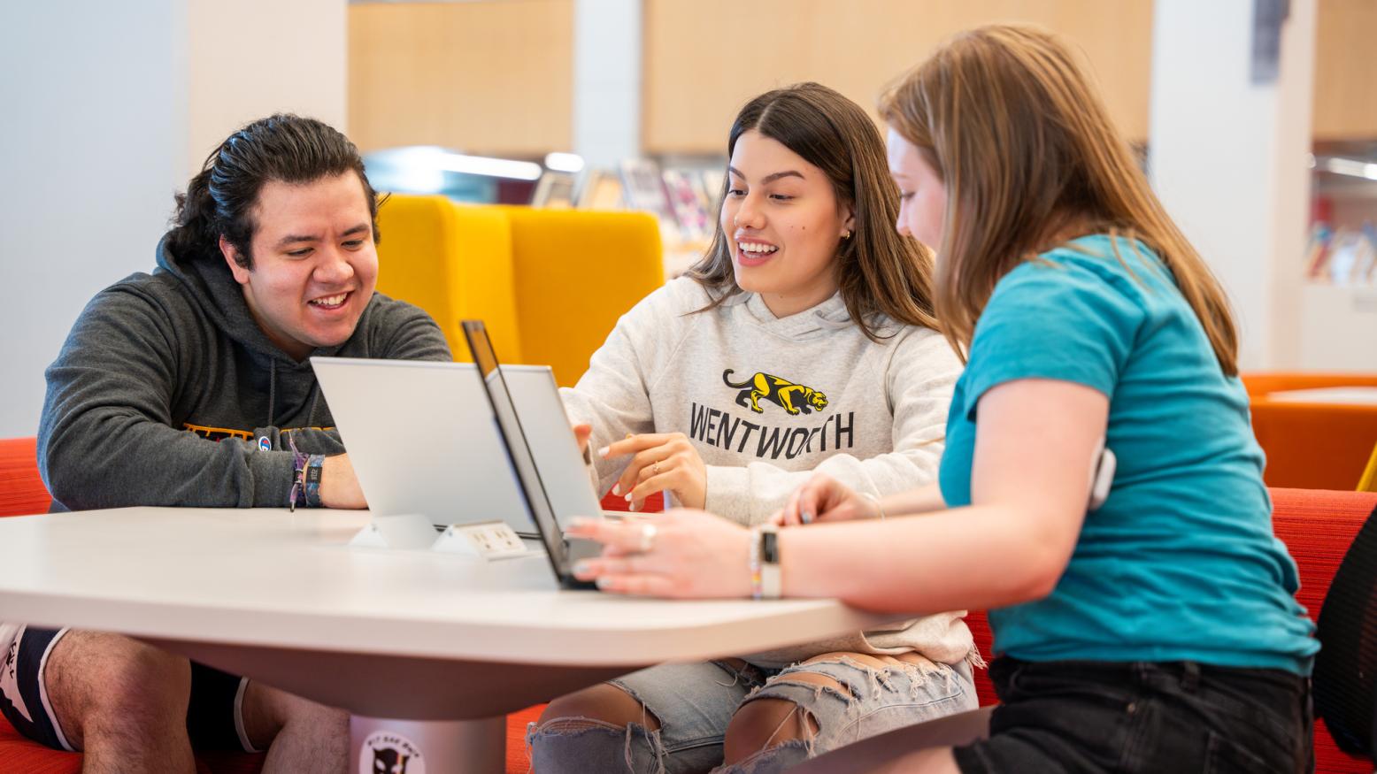 One male and two female students study together with their laptops in the library