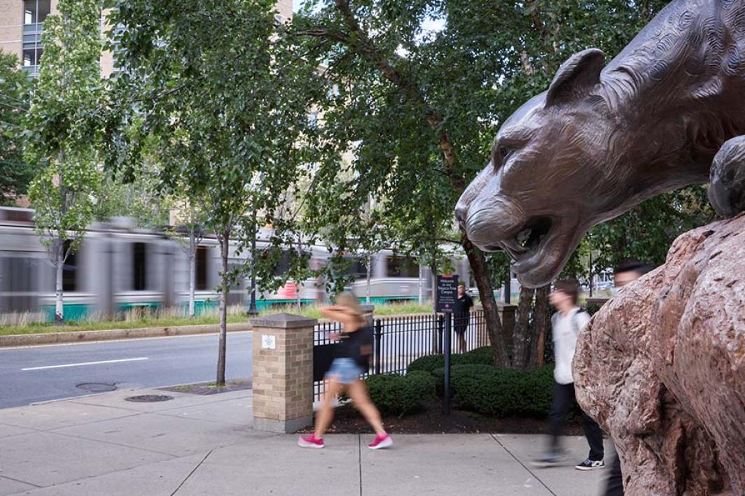 A woman walks past the leopard statue while the T passes in the background.