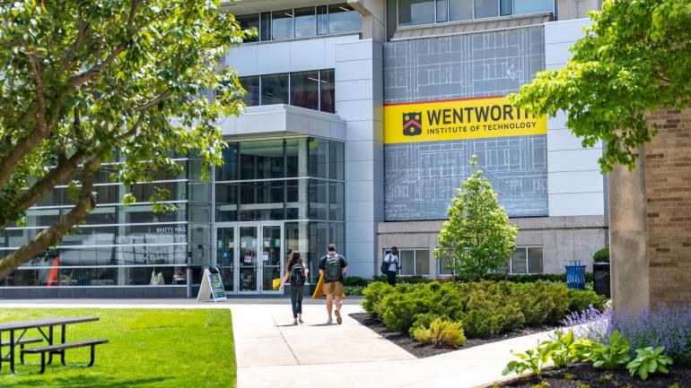 Two students walk towards Beatty Hall in the background with campus greenery in the foreground